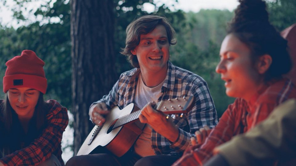 Venner, der synger omkring et bål, mens én spiller guitar